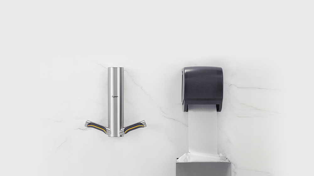Secador de mãos Dyson Airblade 9kJ instalado ao lado de um dispensador de toalhas de papel